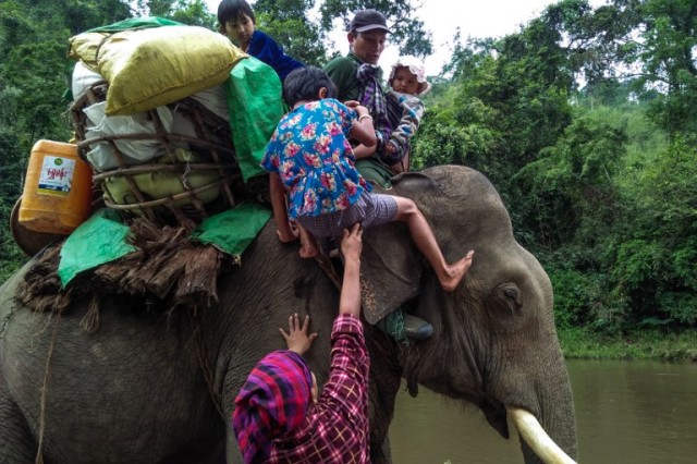 This picture taken on May 2, 2018 shows an internally displaced family getting up on an elephant with their belongings to cross a river