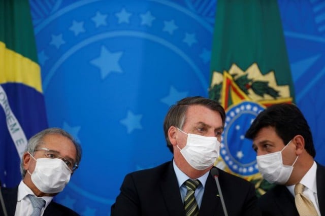 ប្រធានាធិបតីប្រេស៊ីល Jair Bolsonaro (កណ្ដាល), រដ្ឋមន្ត្រីសុខាភិបាល Luiz Henrique Mandetta (ស្តាំ) និងរដ្ឋមន្ត្រីសេដ្ឋកិច្ចប្រេស៊ីល Paulo Guedes នៅសន្និសីទព័ត៌មានមួយ កាលពីថ្ងៃ១៨ ខែមីនា ឆ្នាំ២០២០ (Reuters) 